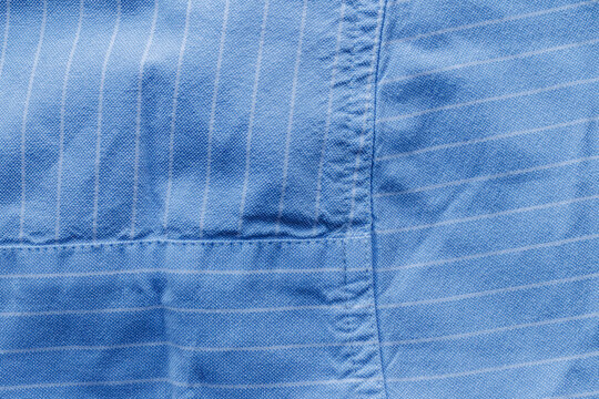 Close-up of blue woven fabric with thin white stripes, overlapping sections, visible stitching, and natural wrinkles.