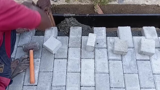 Skilled Mason Using a Hand Trowel to Smooth and Finish Wet Concrete Border Edges Around Interlocking Paving Stones, Manual Construction Work