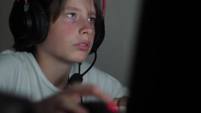 A teenage boy in a large gaming headset intently controls a computer mouse during an intense match. 