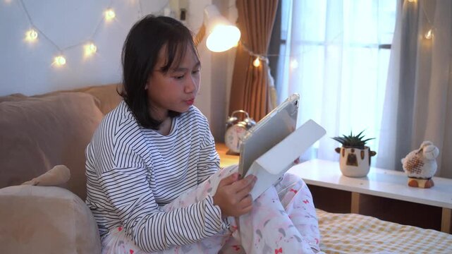 Relaxing Evening, Young girl lies comfortably on bed using leisure time with tablet in a cozy bedroom