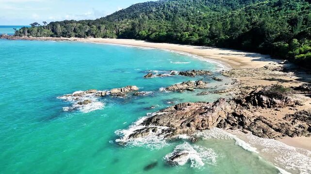 Aerial drone view of a hidden tropical beach with turquoise ocean, granite rocks, lush rainforest and untouched shoreline in bright coastal paradise