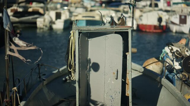 Tilted close up of a fishing boat deck with ropes and equipment, with a marina and waterfront buildings blurred in the background