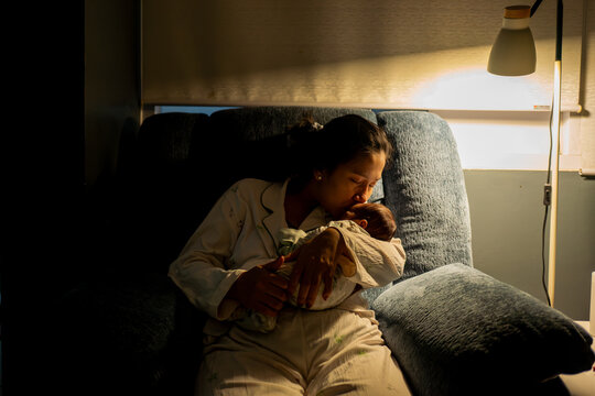 Asian Mother Kissing Her Sleeping Newborn Baby Tenderly at Night