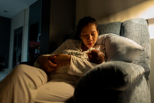 Tender Moment of an Asian Mother Cradling Her Newborn Baby at Night
