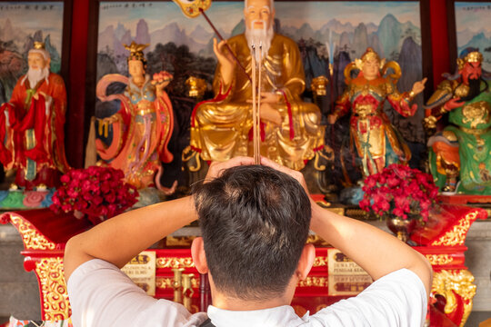 Man Praying with Burning Incense Sticks in Front of Deities at a Chinese Temple