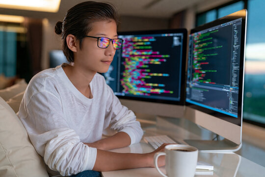 Young software developer coding on multiple monitors in modern home office focused on programming and technology