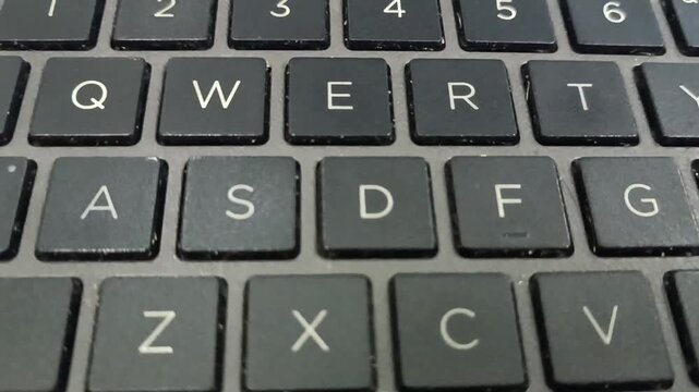 Close-up video of  black laptop keyboard showing QWERTY keys. Focus on letters A to V and numbers 1 to 6. Modern tech detail with matte keys and gray frame.