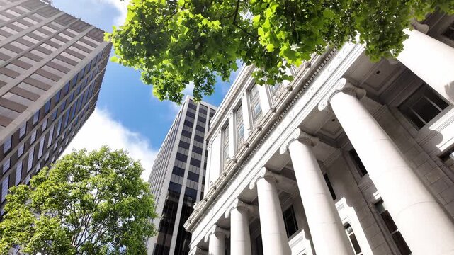 Dynamic wide angle shot captures the historic Old Federal Reserve Bank Building in San Francisco, framed by columns, lush green trees, and modern skyscrapers under bright daylight.