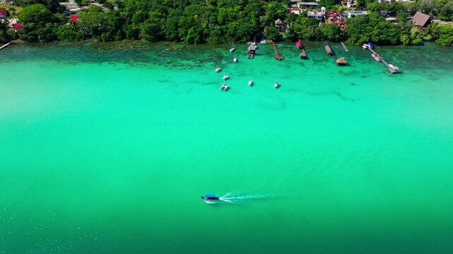 Aerial view of the Bacalar Lagoon shoreline, Quintana Roo, Mexico, lakeside homes and palapas beside turquoise shallows and moored boats.