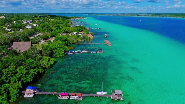 Aerial view of piers, palapas and moored boats along the turquoise Bacalar Lagoon, Quintana Roo, Mexico, lakeside homes among the greenery.