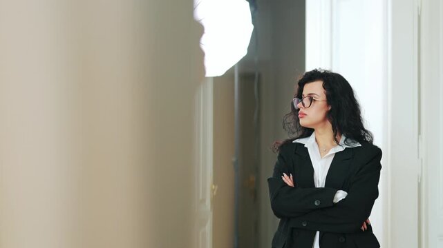 Woman stands with arms crossed, exuding confidence and focus. Thoughtful expression suggests contemplation and determination. Modern style with power suit and glasses conveys competence and strength.