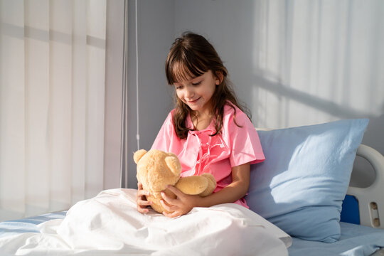 Caucasian young girl sitting on a hospital bed, holding her teddy bear. 