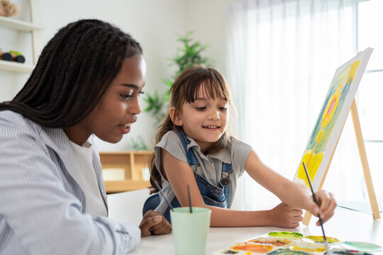 African woman tutor guide young child through art and painting in nursery. 