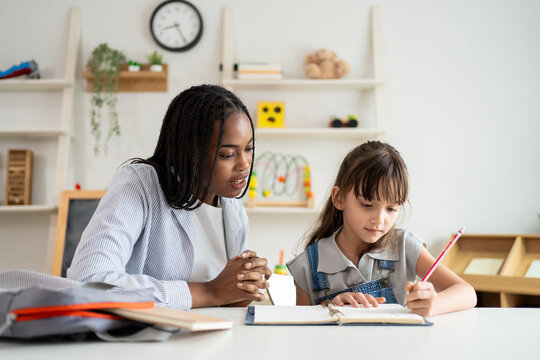 African woman tutor guide young child through learning activities on table.