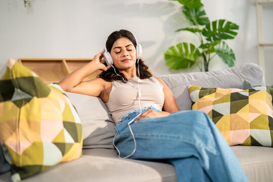 Indian beautiful woman listen to music while sitting on sofa in house. 