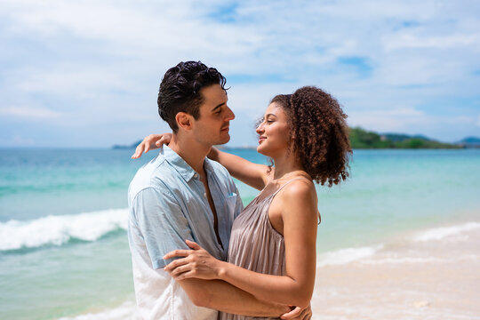 Caucasian young man hugging his Latina girlfriend on a sandy beach. 