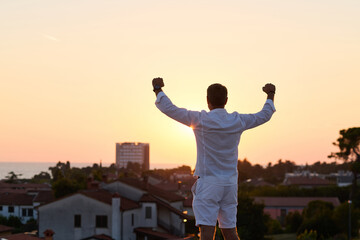 Obraz premium Man Celebrating On Rooftop Terrace At Sunset Over Seaside Town With Balcony View