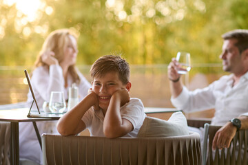 Obraz premium Family Relaxing on Balcony Terrace Overlooking Sea With Smiling Boy in Summer Evening
