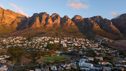 Naklejka premium Evening view of Camps Bay, South Africa, as dusk settles over the Atlantic coastline. The Twelve Apostles mountain range glows in the fading light, creating a breathtaking coastal scene.