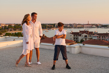 Obraz premium Family On Rooftop Terrace With Sea View At Sunset Over Coastal Town