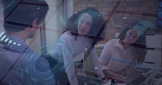 AR HUD appearing, standing woman leaning, gesturing and seated peer scanning laptop, reviewing data