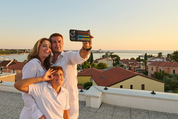 Obraz premium Family Taking Selfie on Rooftop Balcony With Sea View at Sunset in Coastal Town