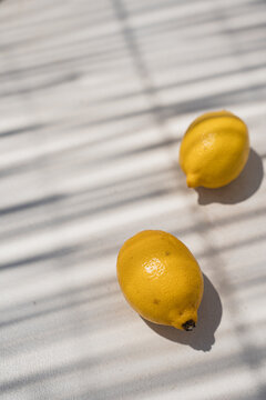 Two Fresh Yellow Lemons On Light Surface With Window Blind Shadows