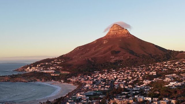 Aerial drone view over Camps Bay, Cape Town, at sunset. The Atlantic coastline, golden evening light and Lion's Head in the background create one of South Africa's most iconic coastal landscapes.