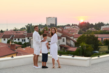 Obraz premium Family On Rooftop Terrace At Sunset Over Coastal Town Sea View
