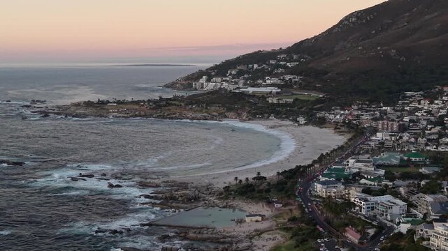 Aerial drone view over Camps Bay, Cape Town, at sunset. The Atlantic coastline, golden evening light and Lion's Head in the background create one of South Africa's most iconic coastal landscapes.