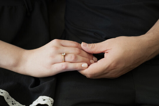 Couple holding hands with engagement ring, symbolizing love and commitment in a romantic setting.
