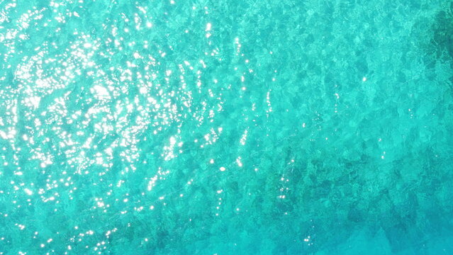 Aerial top down view of turquoise to deep blue sea water texture with sun rays reflection