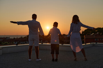 Obraz premium Family Holding Hands on Rooftop Terrace at Sunset With Sea View and Silhouettes