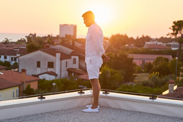 Obraz premium Man Standing On Rooftop Balcony At Sunset Overlooking Sea View And Coastal Town For Vacation