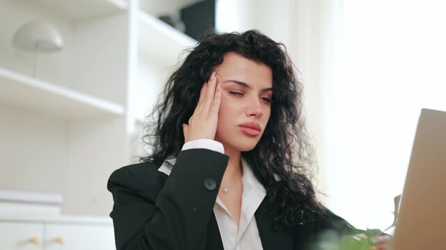 Concentrating on laptop, young woman experiences a sudden, painful headache. The strain of work from home leads to discomfort, showing feelings of frustration and distress.