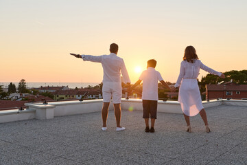 Obraz premium Family Holding Hands on Rooftop Terrace at Sunset With Sea View and Summer Vibes