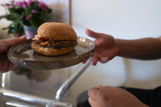 A person handing over a delicious cheeseburger on a plate, perfect for food lovers and fast food promotions.