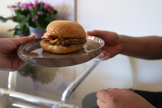 Delicious hamburger being served on a plate, showcasing a sesame seed bun and toppings in a cozy dining environment.