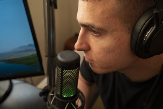 Man with headphones using a microphone while focused on a computer screen in a home studio setting.