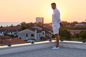 Obraz premium Man Standing on Rooftop Terrace at Sunset Over Coastal Town Sea View and Relaxation