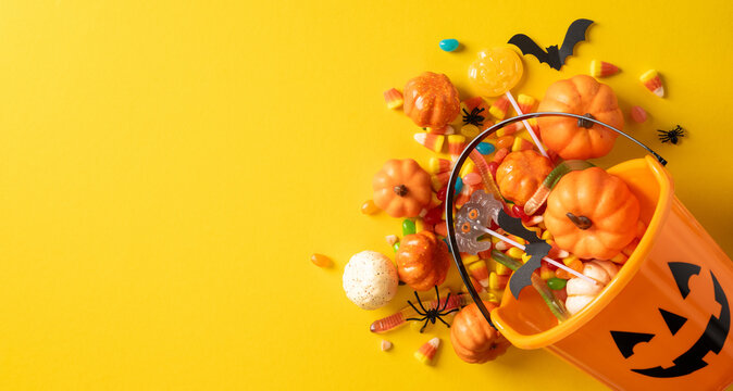 Happy Halloween pumpkin bucket spilling candy and decorations on banner yellow background