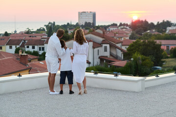 Obraz premium Family on Rooftop Terrace Watching Sunset Over Seaside Town From Balcony of Holiday Home