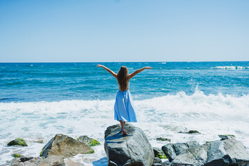 Woman stands on rock by ocean while waves crash during bright day at the beach © DSMT