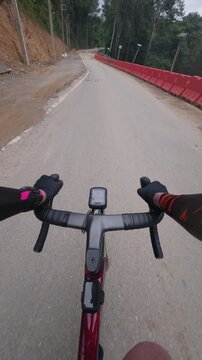 First-person point of view of a road cyclist riding along a mountain road with muddy patches and challenging surface conditions. Surrounded by tropical forest, the footage highlights endurance cycling