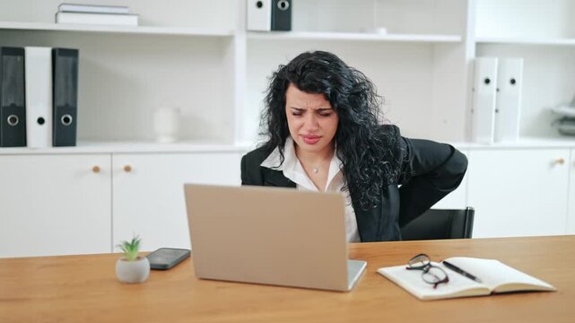 Professional businesswoman experiencing severe back pain while working at office. Long hours and sedentary work lead to discomfort and suffering. Common health issue in modern corporate environment.