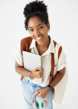Top view of smiling young female student holding laptop and pink headphones looking at camera in studio