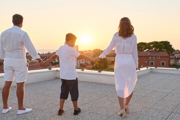 Obraz premium Family Holding Hands on Rooftop Terrace at Sunset With Sea View and Summer Vacation Moment