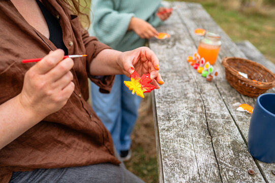 Adult hands painting ceramic maple leaf during outdoor craft activity