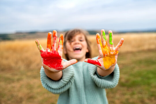 Child girl showing colorful painted hands outdoors