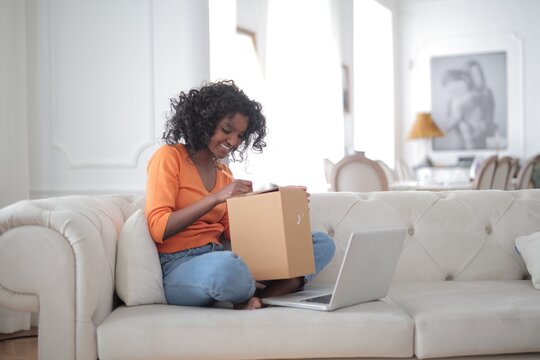 Happy woman preparing a package for shipping on couch